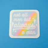 Square vinyl sticker with rounded corners that reads not all men but always a man in white script with decorative white sparkles. The background of the sticker is pale blue with pastel rainbow stripes running diagonally from top-right to bottom-left. The sticker has a white border.