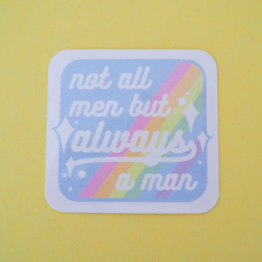 Square vinyl sticker with rounded corners that reads not all men but always a man in white script with decorative white sparkles. The background of the sticker is pale blue with pastel rainbow stripes running diagonally from top-right to bottom-left. The sticker has a white border.