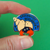 Semi-circular, blue enamel pin with the image of a hermit crab in a peach coloured spiral shell. Only the crabs eyes and red claws are visible, peeking out from the darkness of the shell's entrance. The words Exclusively Reclusive are written on the blue section in silver capital letters with some silver sparkles. The pin is being held between a thumb and forefinger in front of a green background.