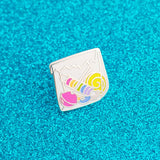 Enamel pin in the shape of a paper bag full of brightly coloured sweets.  Pin is on a glittery blue background.