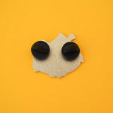 The back of an enamle pin with two black rubber backings. The pin is on a yellow background.