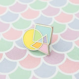 Enamel pin featuring an overlapping circle, square, and triangle. The shapes are pastel coloured, with the colours mixing where they overlap. The pin is shown on a pastel, fish-scale patterned background.