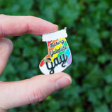 Enamel pin in the shape of a Christmas stocking with rainbow stripes, it reads Making Yuletide Gay in black script. The word Gay is larger and has star sparkles. The pin is held between a forefinger and thumb.