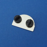The back of a semi-circular enamel pin with two black rubber backings. The pin is on a blue background.