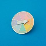 A circular pin with a spinning arrow which reads Anxiety. The main body of the pin is split into 8 pastel-coloured sections. They are labelled; Recession, Pandemic, Something I Said 2 Years Ago, Inequality, Existential Dread, Climate Change, The Patriarchy, Politics.