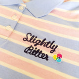 Enamel pin with three overlapping circles. The circles are filled cyan, magenta, and yellow; with the colours mixing in the areas where they overlap. Pin is on a pastel striped polo shirt next to the embroidered words Slightly Bitter.